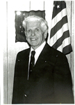 White haired man in front of American flag