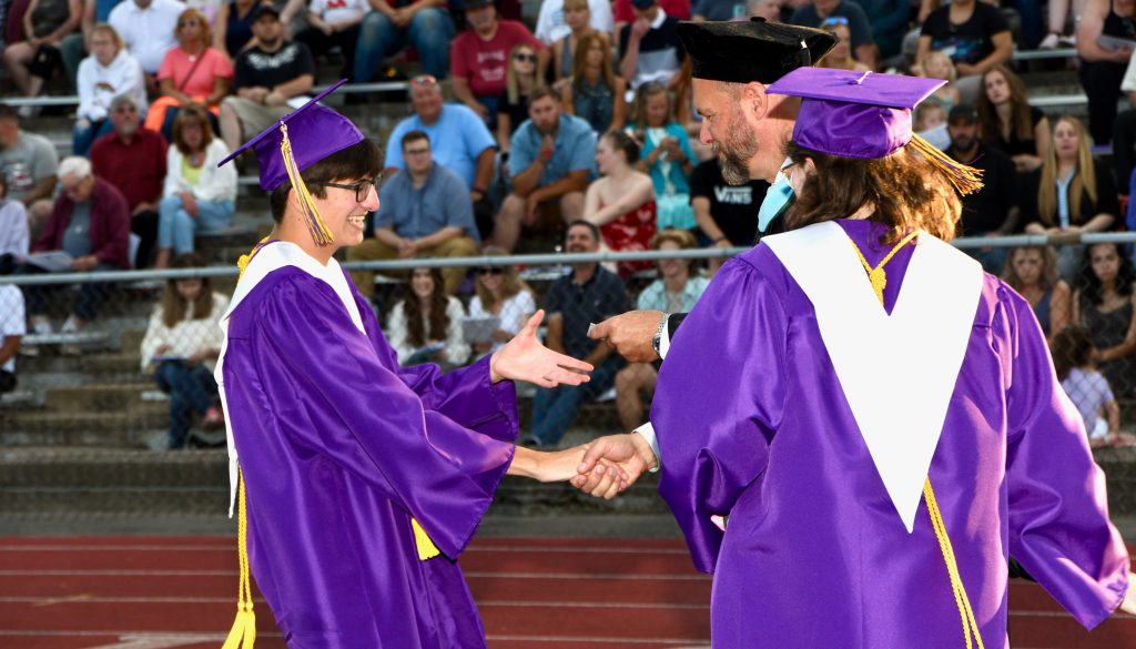 A student shakes the Superintendent's hand and reaches for his diploma at graduation