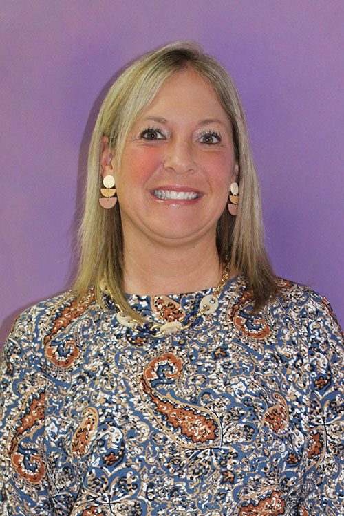 Amy Hale smiles broadly in front of a purple background