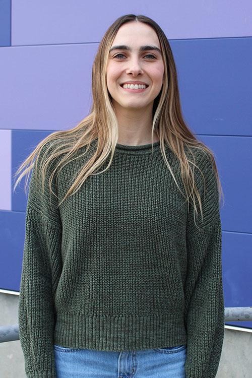 Ashley Polidore smiles broadly in front of a purple wall