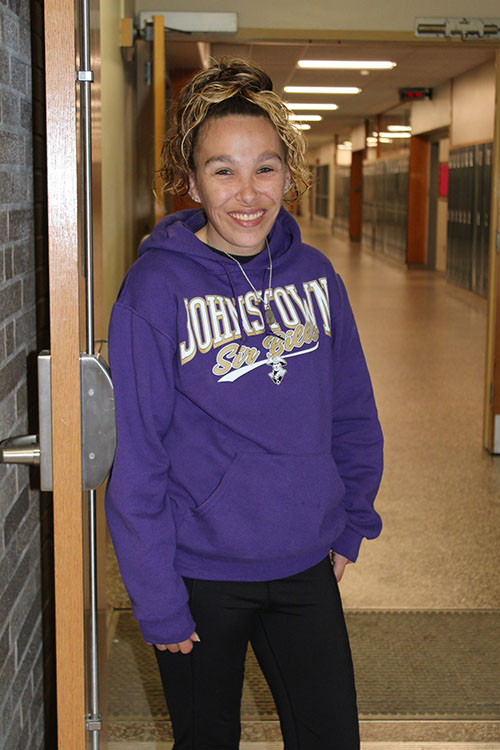 Catherine Darling stands in a hallway wearing the purple and gold Johnstown sweatshirt