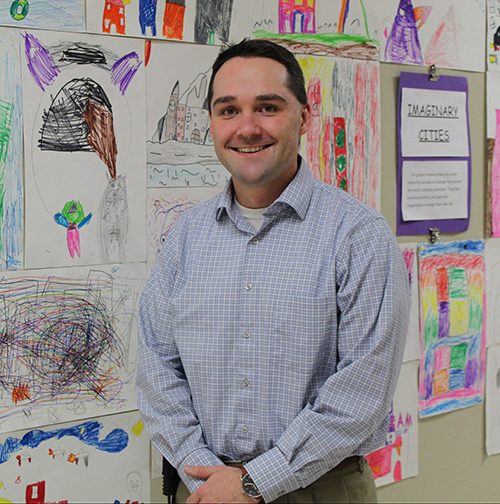 Dr. Chad Swanson stands in front of a wall covered with children's artwork