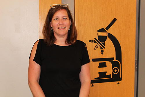 Portrait of Heidi Bolebruch next to a large wall decal of a microscope