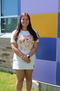 a young teen girl wearing a white shirt and top poses outside of a school