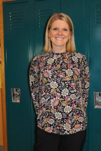 a woman wearing a floral shirt stands in front of school lockers