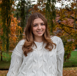 a brunette teenaged girl wears a white sweater outdoors