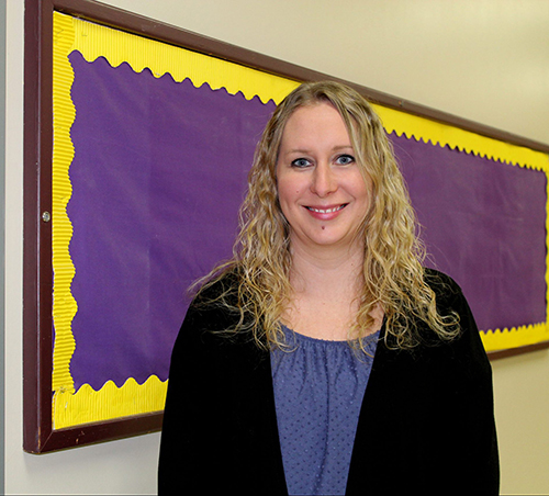 Jessica Holt stands in front of a purple and gold bulletin board