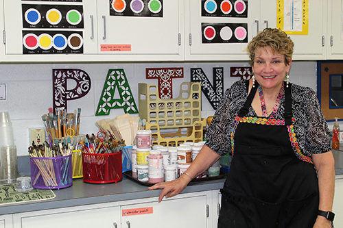 Art Teacher Julia Fisk poses in front of a counter filled with art supplies