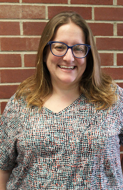 Karlene Peck smiling, stands in front of brick wall