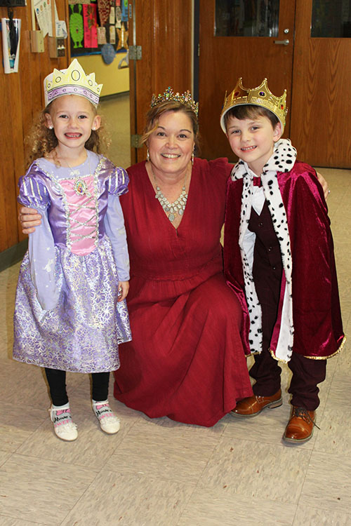 Melissa Livingstone wearing a crown, kneels down between two students dressed as a prince and princess