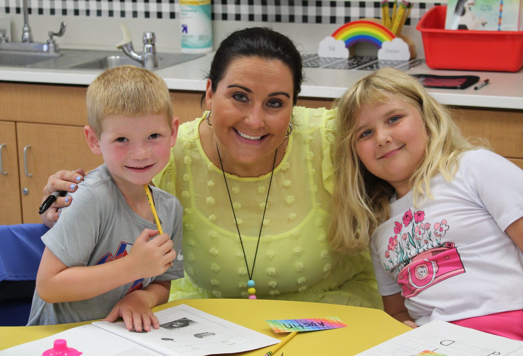 A teacher poses with two students working at a table