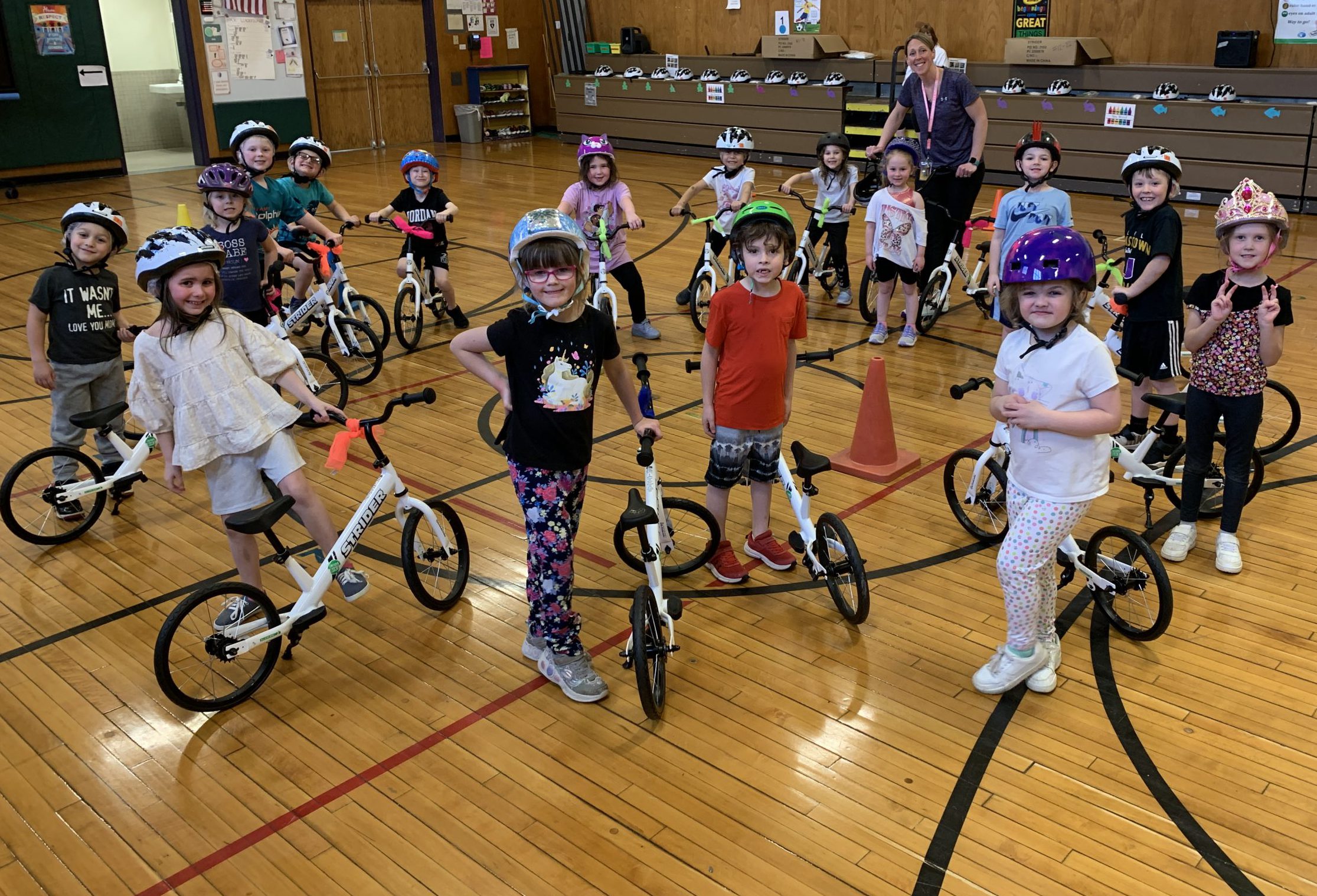 Several students wearing bike helmets gather in a circle with their bikes in the gymnasium