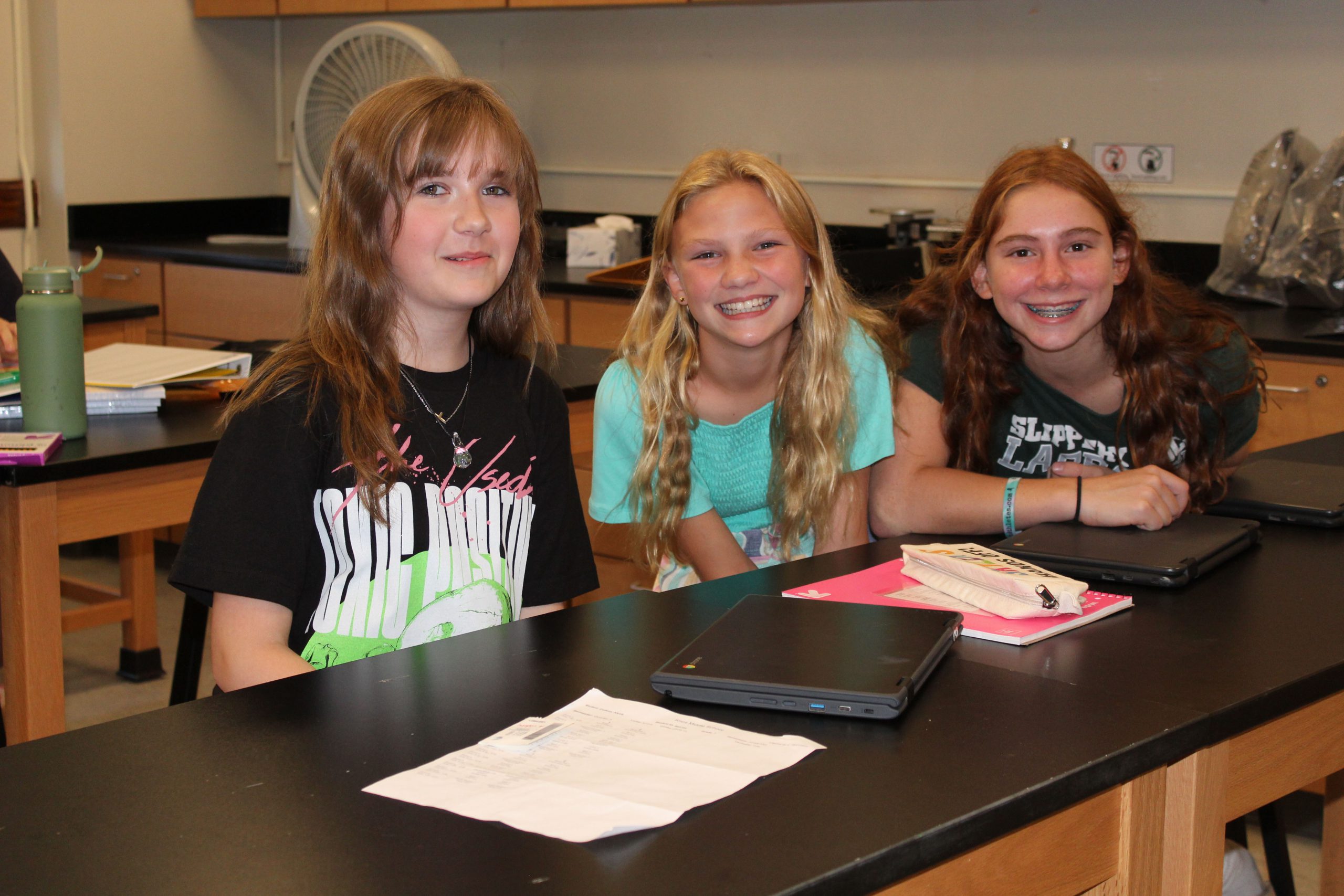 Three students smile together in a classroom