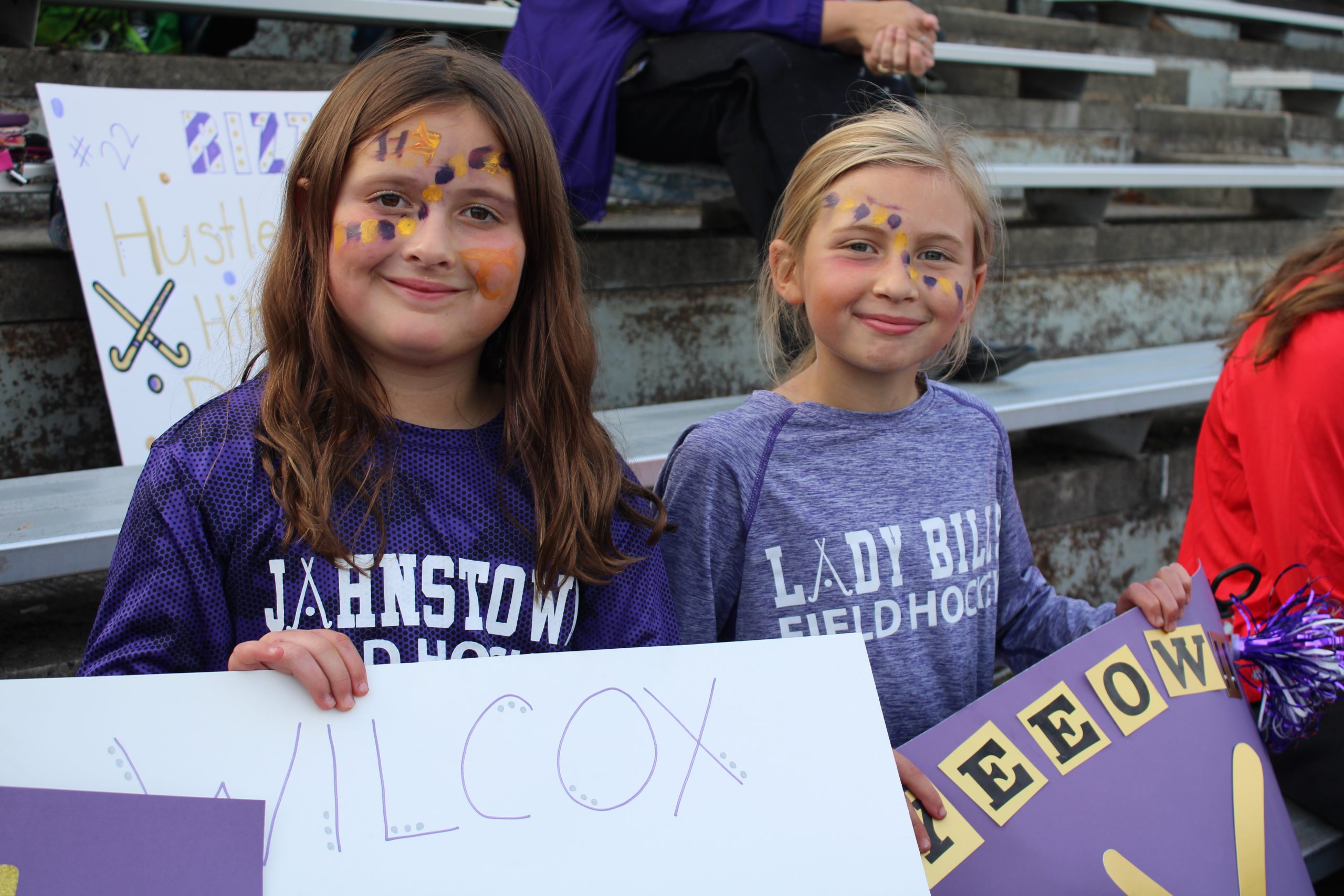 Two students wearing purple hold handmade cheering signs at a game