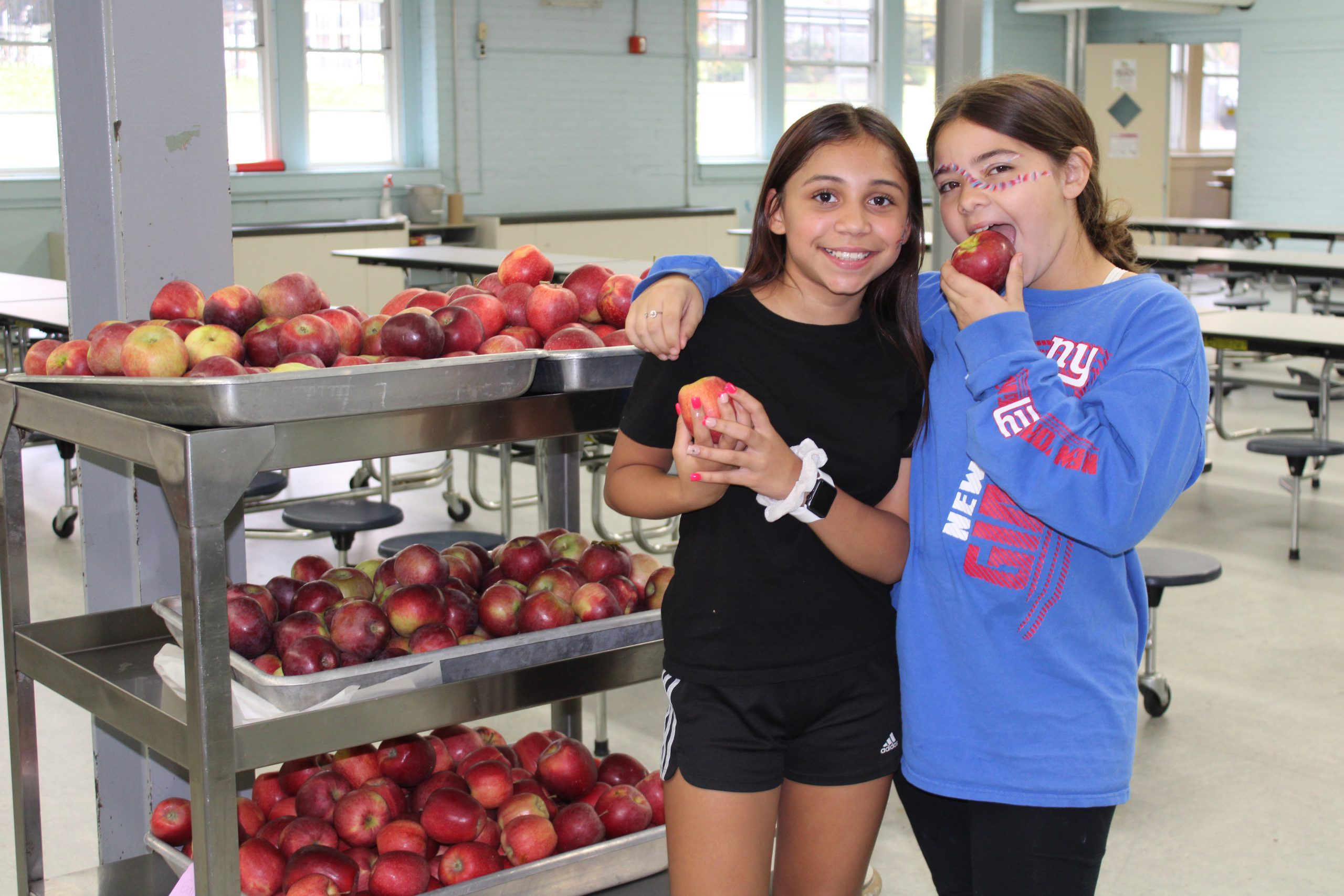 Two students stand with trays of apples in the cafeteria