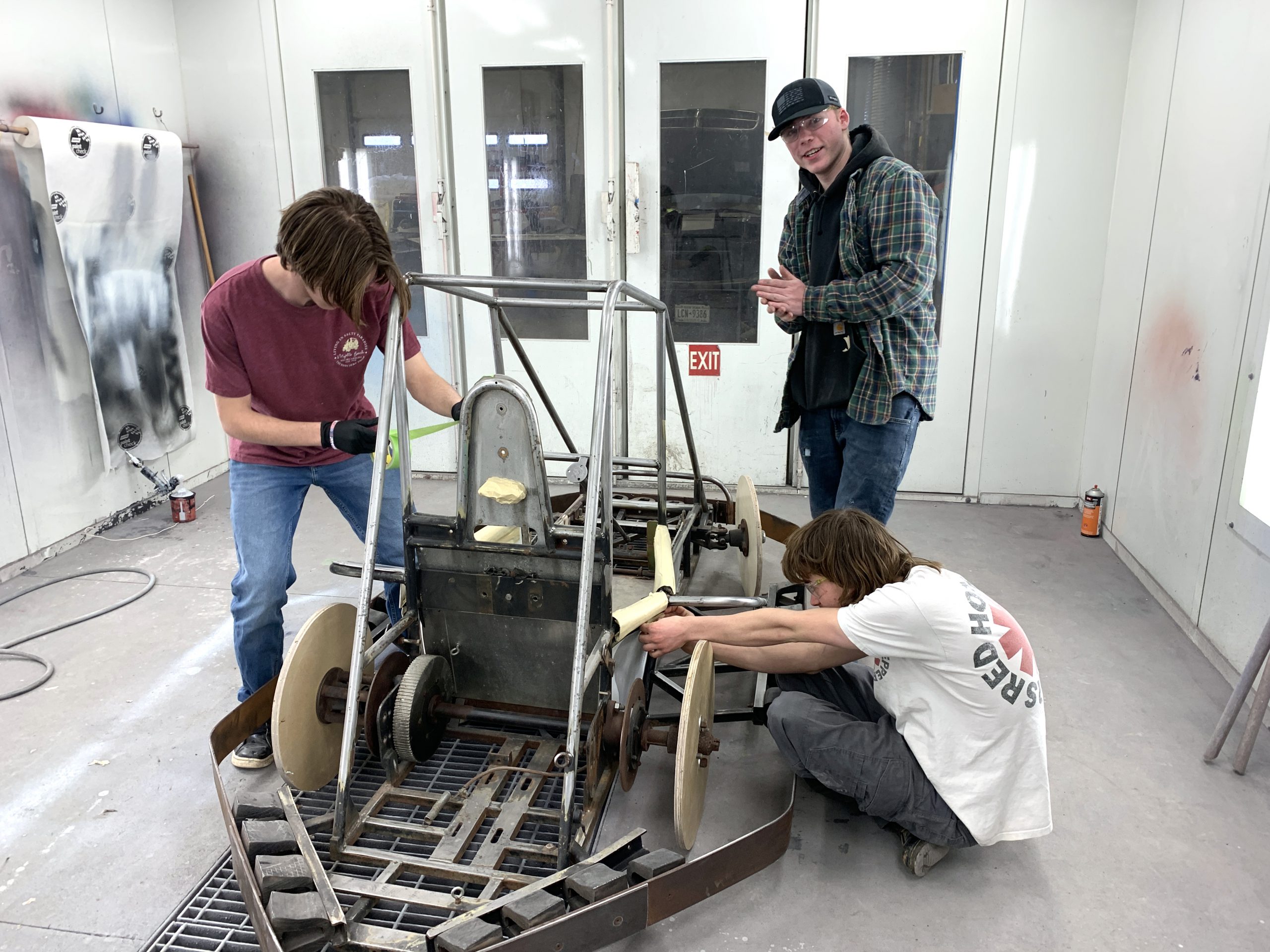 Three CTE students work on a constructed four wheel vehicle