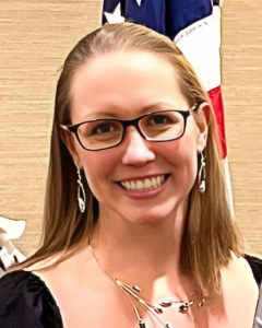 Stephanie Visconti, wearing black glasses, smiles in front of an American flag