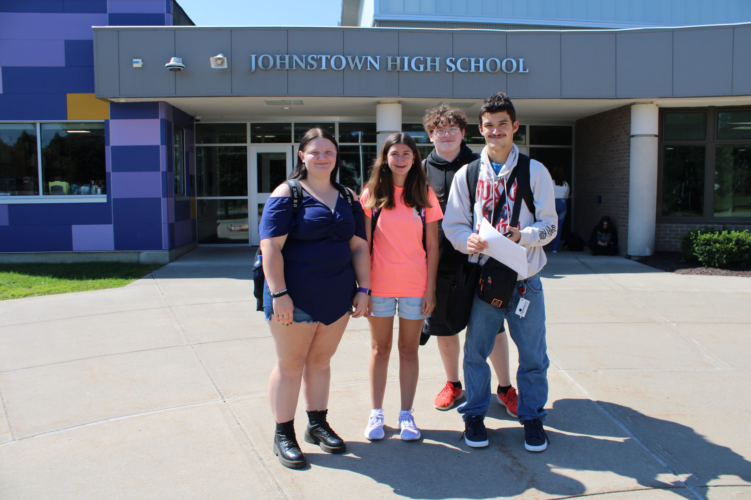 four students stand in front of a school building