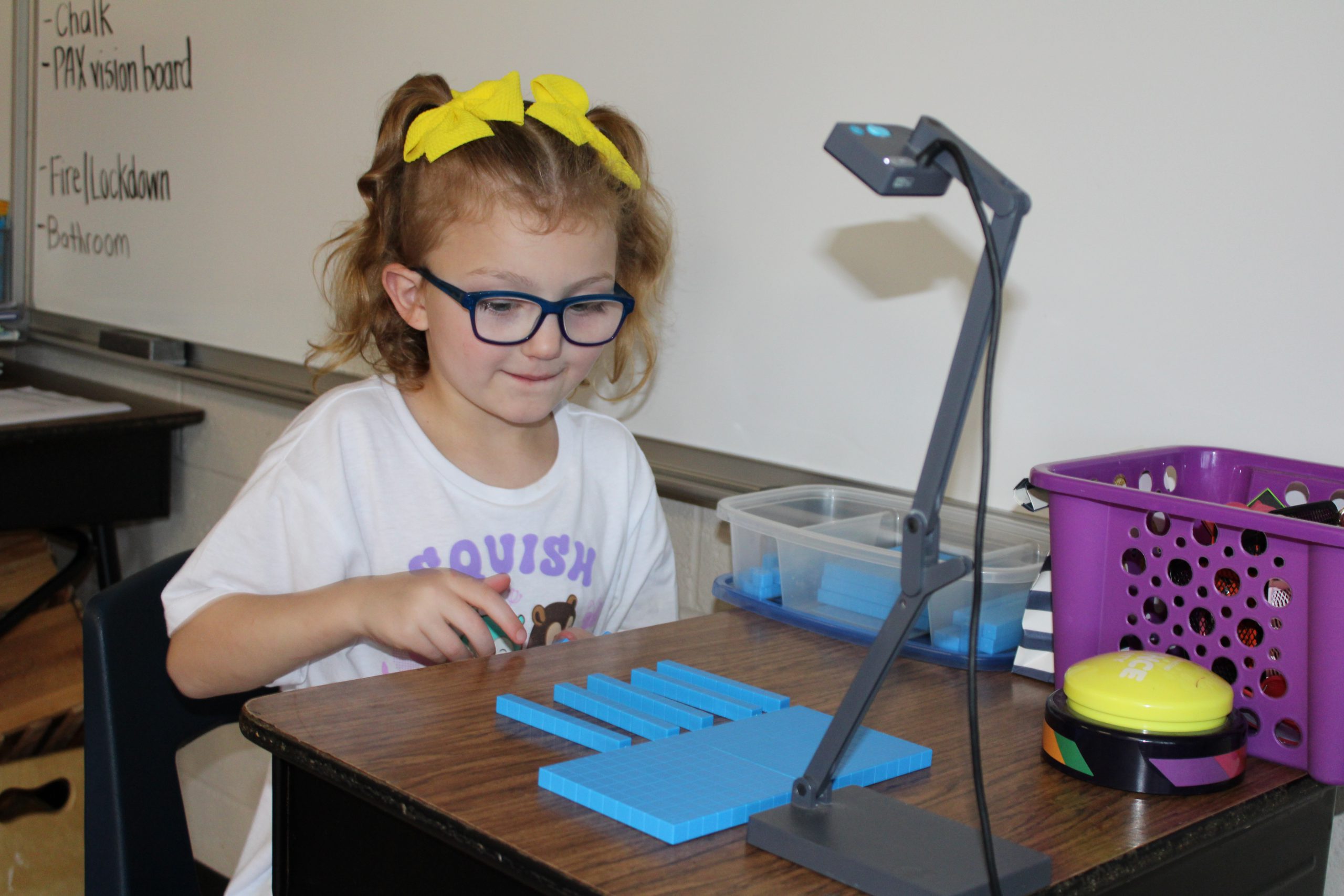 a young girl wearing a yellow bow and glasses arranges blue tiles on a desk