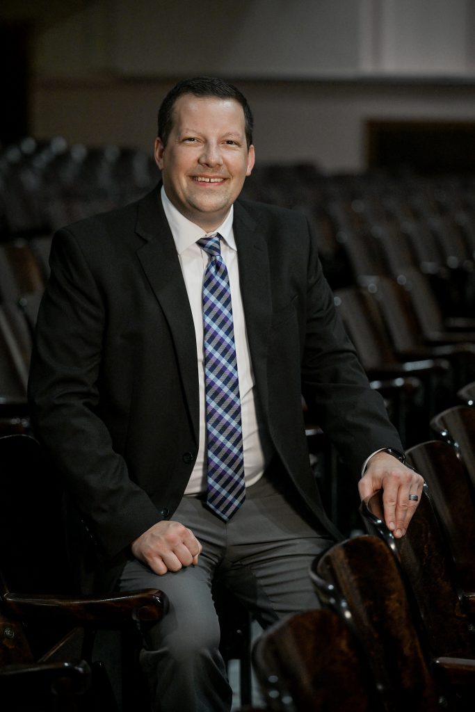 a man wearing a suit and tie sits in an empty auditorium