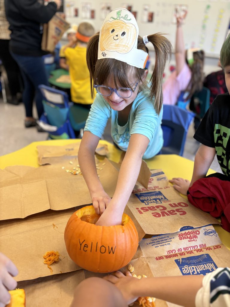 a young girl wearing a hat and classes reaches her hand into a pumpkin