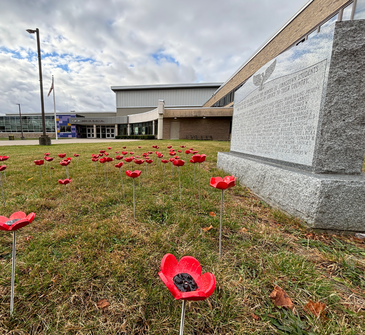 a stone monument is surrounded by red poppies with a school building in the background