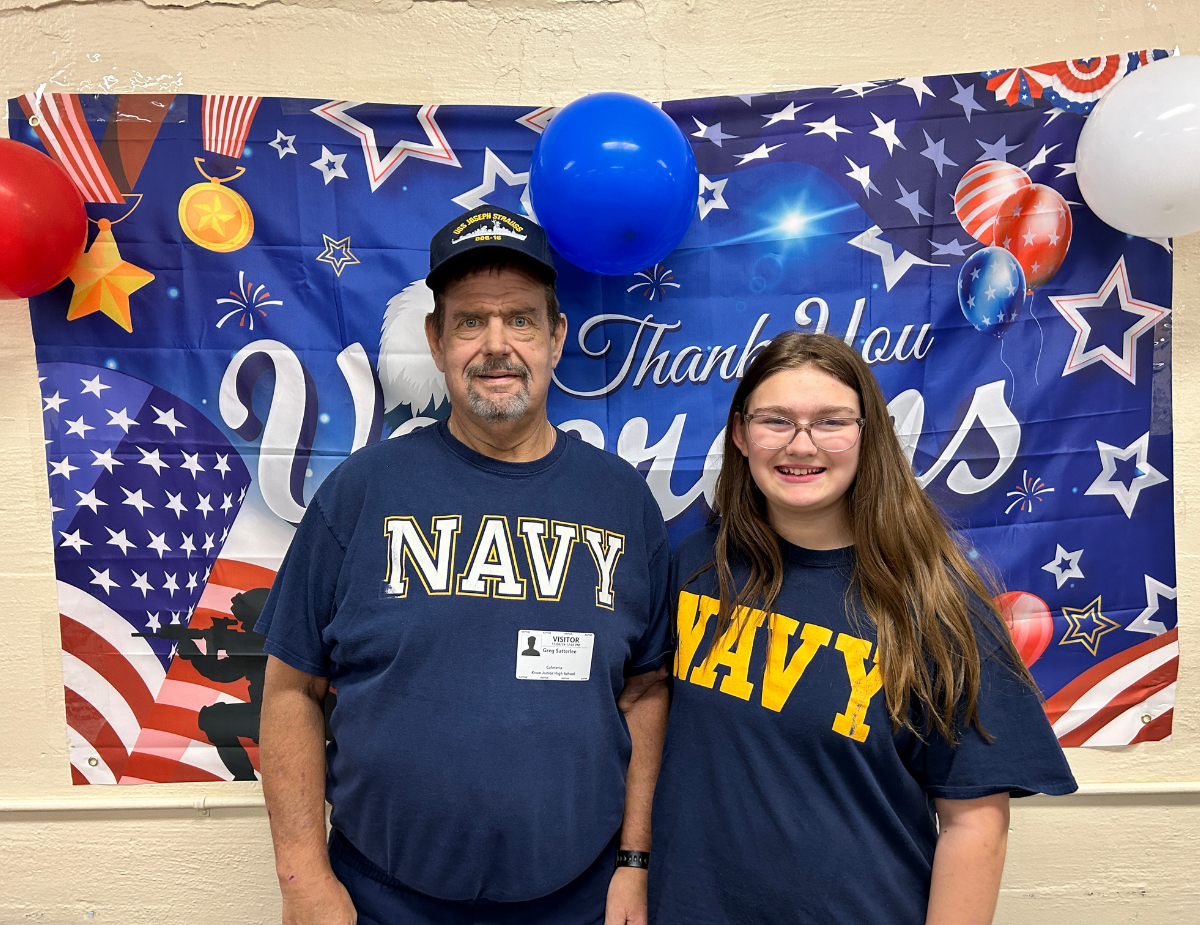 a man and a young girl pose in front of a banner wearing Navy t-shirts