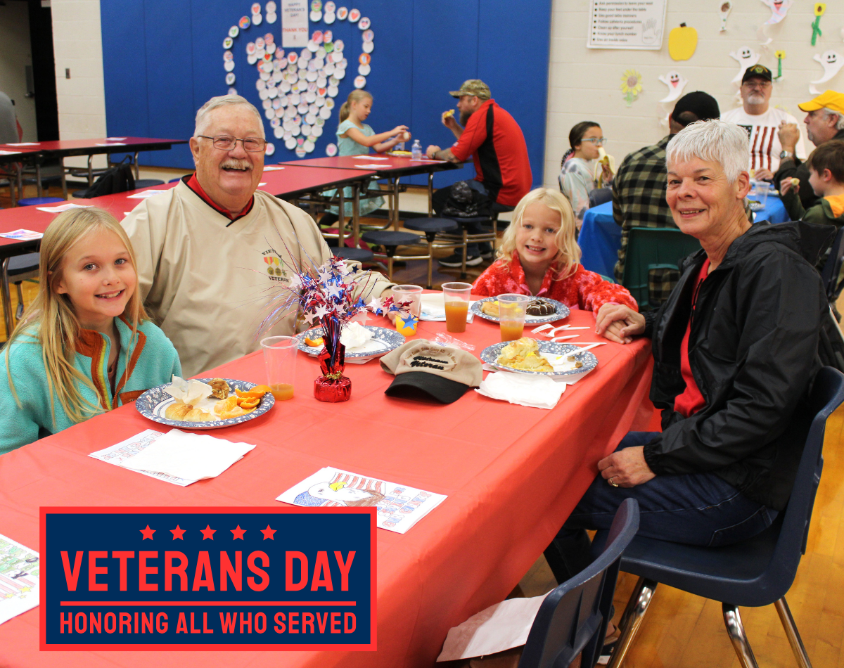 two older adults sit at a table to eat breakfast with two young girls in honor of veterans day