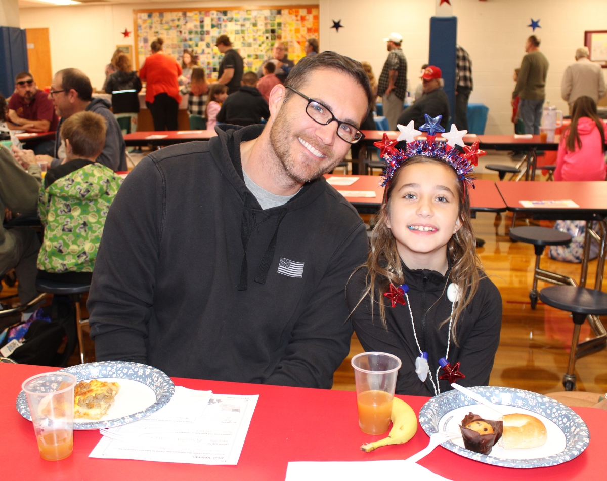 an adult male sits down to eat breakfast with a young girl in honor of veterans day