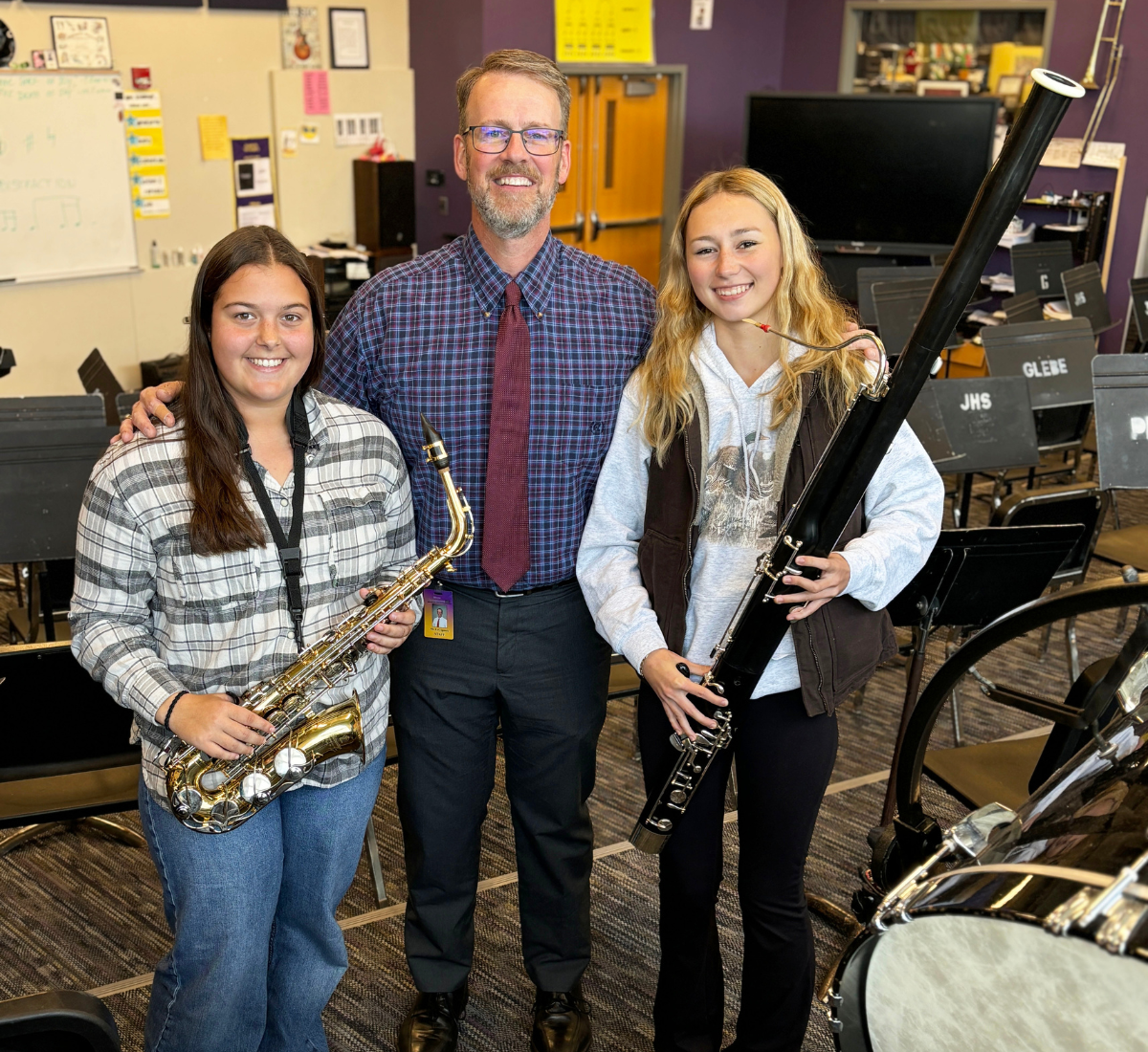 two young ladies pose holding instruments, next to their music teacher