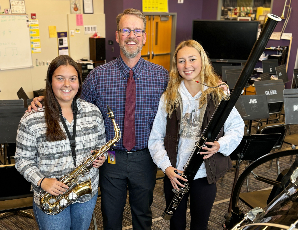 two teenage young ladies pose with their instruments and their music teacher