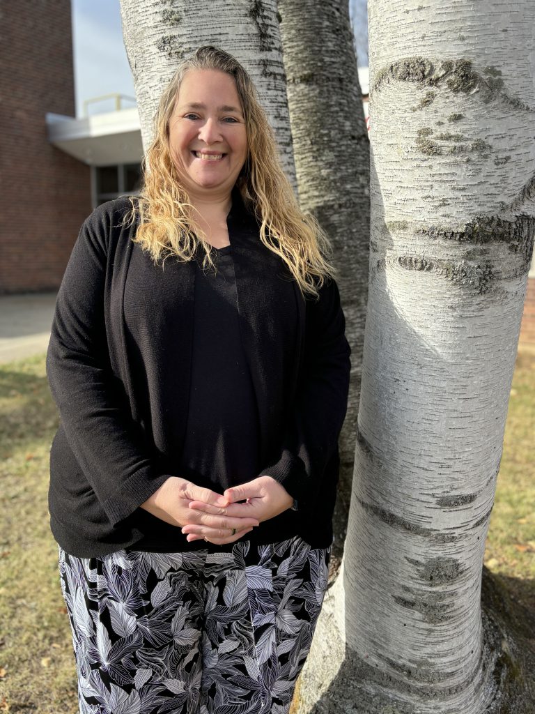 a woman stands outside next to a white birch tree