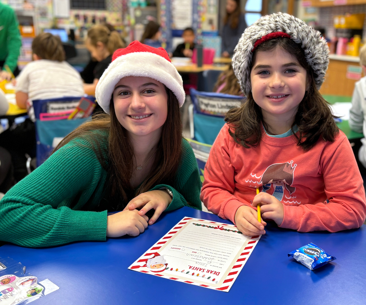 a teenaged girl in a santa hat poses with a young girl in a santa hat