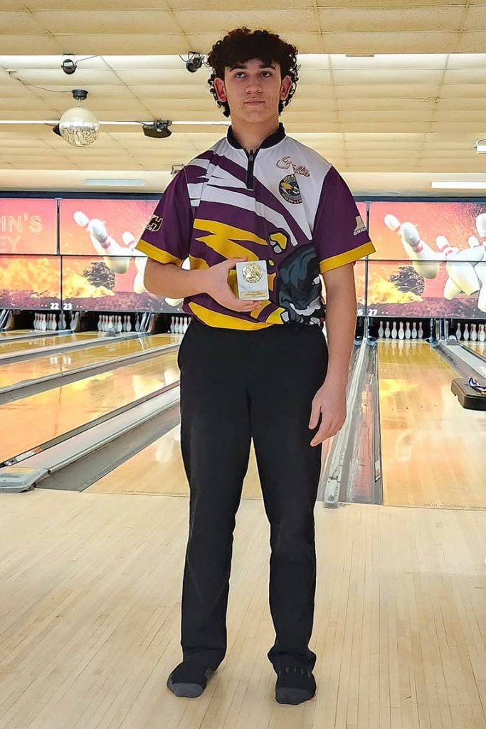 a young man poses on a bolwling lane holding a plaque