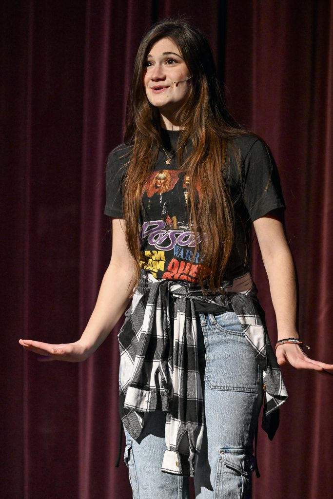 a girl wears a tshirt and jeans as she sings a song on stage