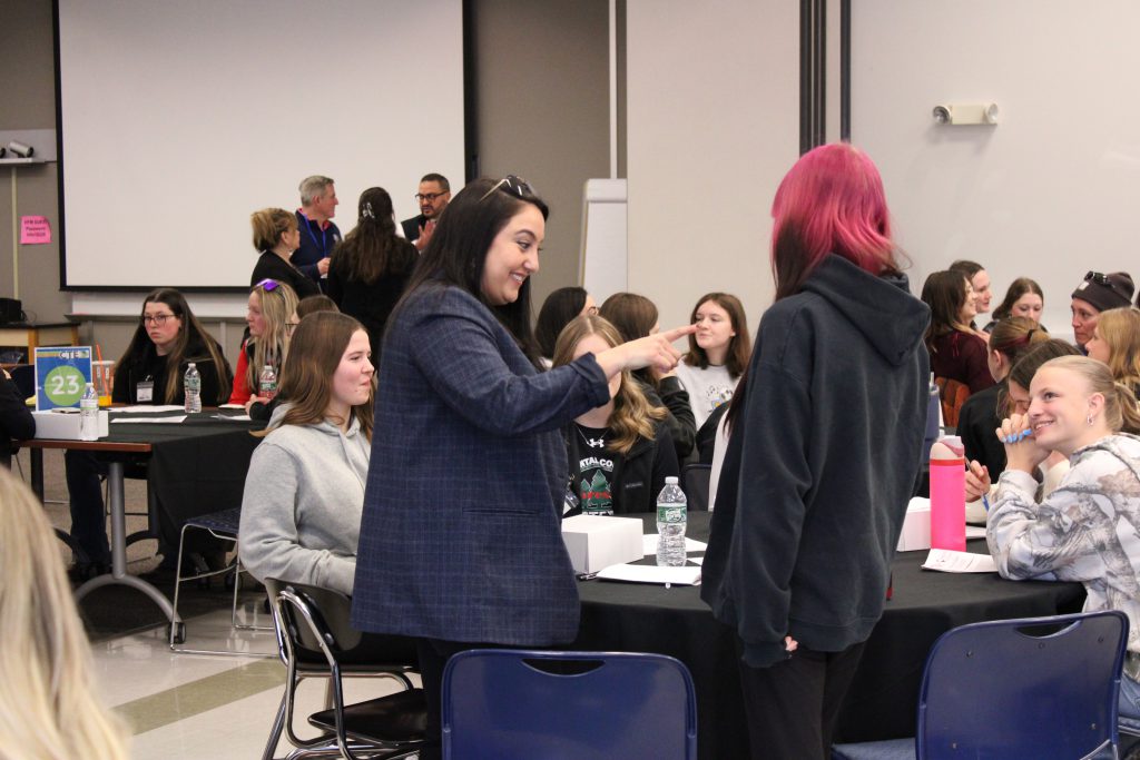 an adult woman points at a young female with pink hair