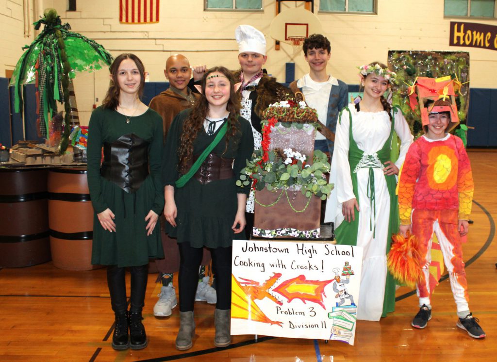 students pose in costume in front of props in a gymnasium