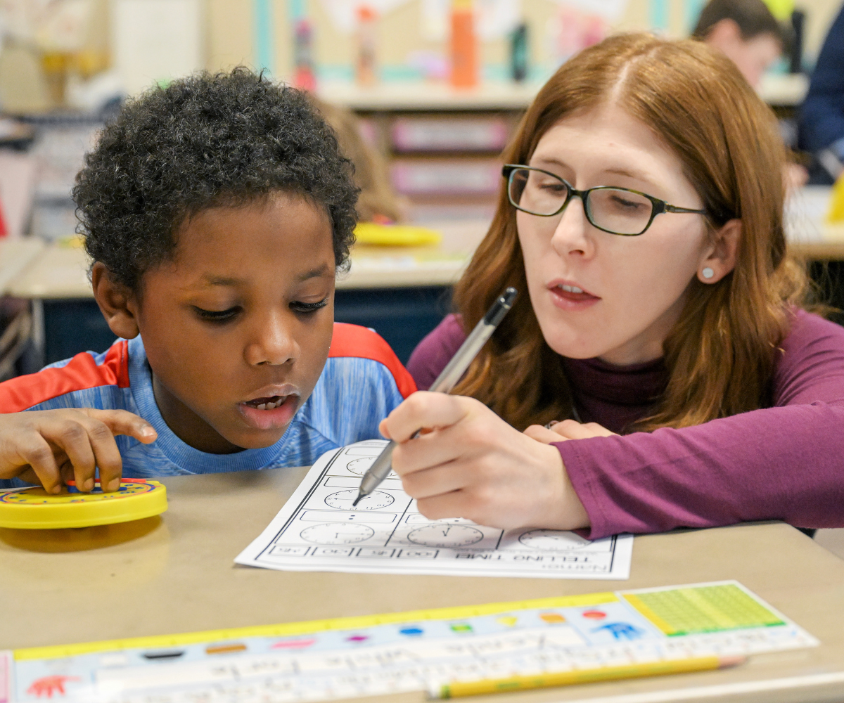 a teacher helps a student learn how to tell time