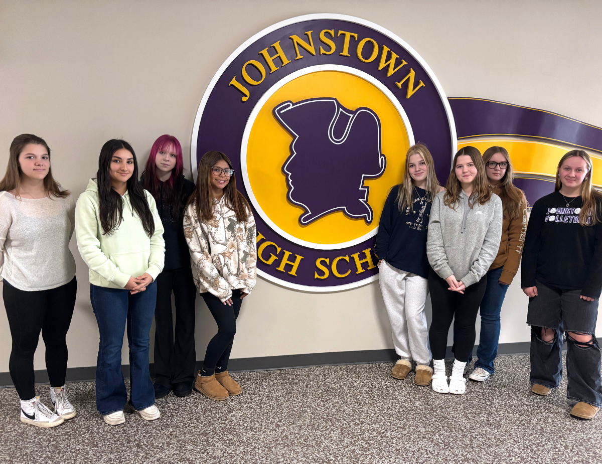 a group of eight young women stand in front of their HS logo